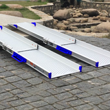 Heeve Aluminium Telescopic Mobility Ramps with blue handles and perforated anti-slip surfaces extended over a raised stone edge outdoors, illustrating their adaptability and secure design for uneven surfaces in natural settings