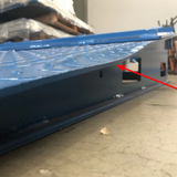 Side view of a blue steel ramp with a minor dent, indicated by a red arrow.