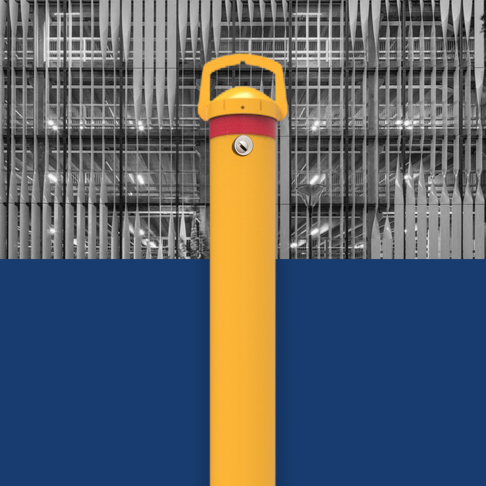 Yellow removable bollard with red reflective band and lock mechanism in front of a building with a modern architectural facade