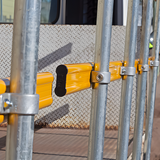 Close-up of an orange guardrail mounted on a flatbed truck, secured with metal clamps.