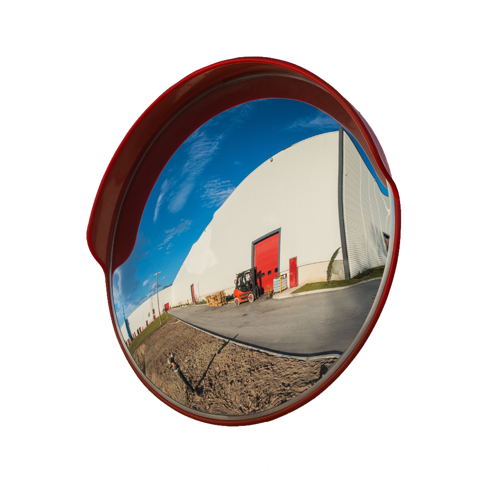 A convex mirror with a red border, mounted outdoors, reflecting the view of a building and surrounding pavement. The mirror showcases its wide-angle reflection capability