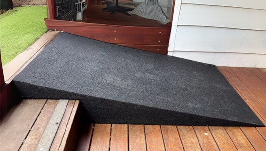 A black carpeted accessibility ramp installed on a wooden deck, providing a smooth transition from an elevated indoor space to the outdoor area