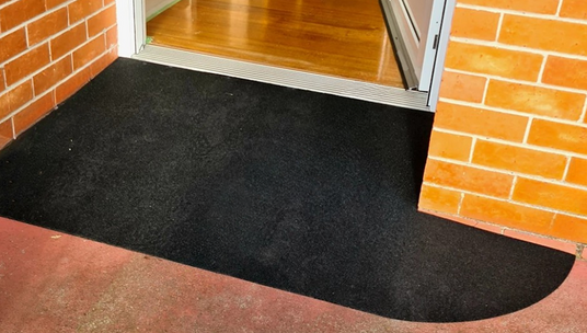 A custom-made black rubber threshold ramp placed at a doorway, offering seamless wheelchair and mobility aid access over a small step.