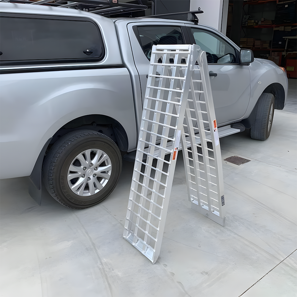 Reinforced aluminium loading ramps folded and standing upright beside a silver pickup truck, showcasing their durability and strength