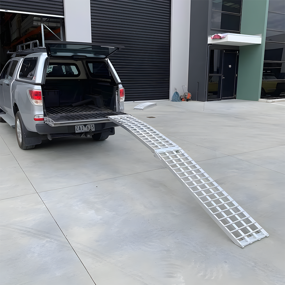 Reinforced aluminium loading ramp attached to the tailgate of a pickup truck, extended at an incline, ready for heavy-duty loading