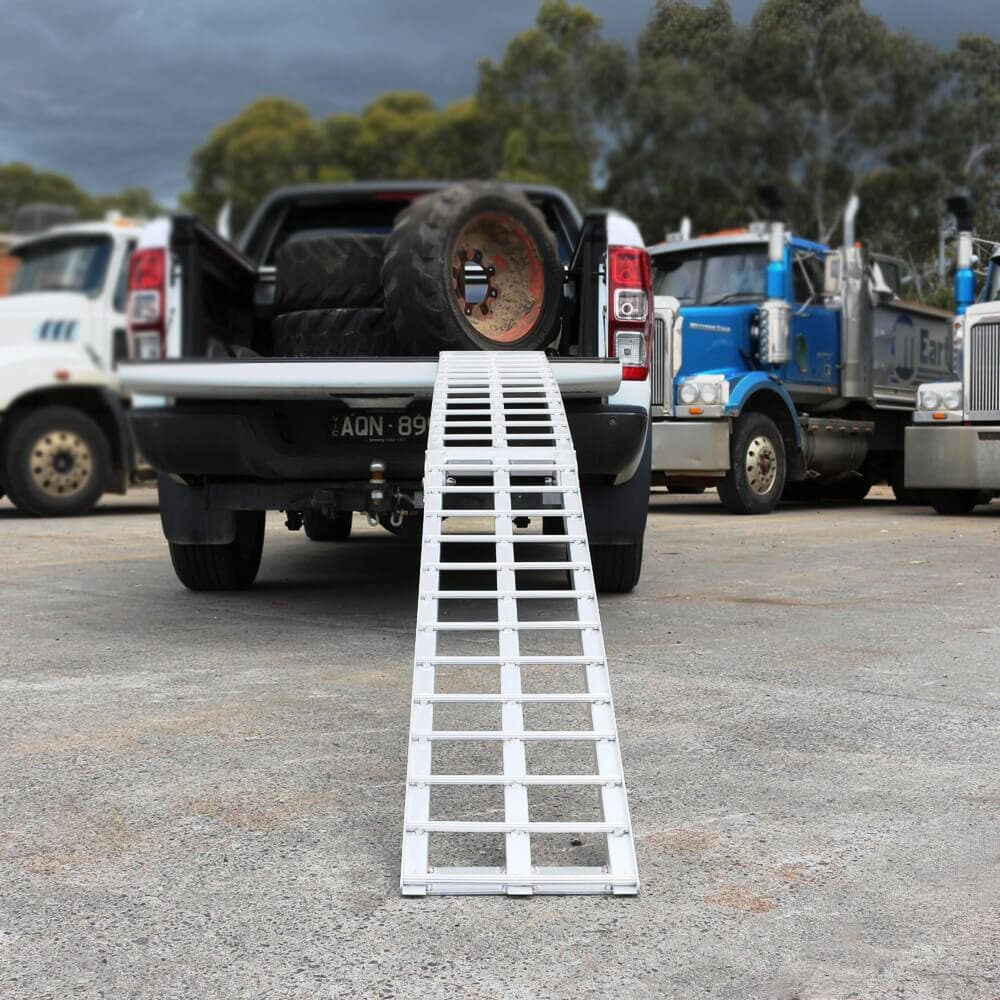 Aluminium loading ramp extended from the tailgate of a pickup truck loaded with large tires