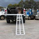 Aluminium loading ramp extended from the tailgate of a pickup truck loaded with large tires