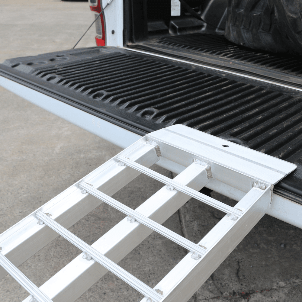 "Close-up of a standard aluminium loading ramp securely placed on the tailgate of a pickup truck, showing the ramp's sturdy build and attachment."