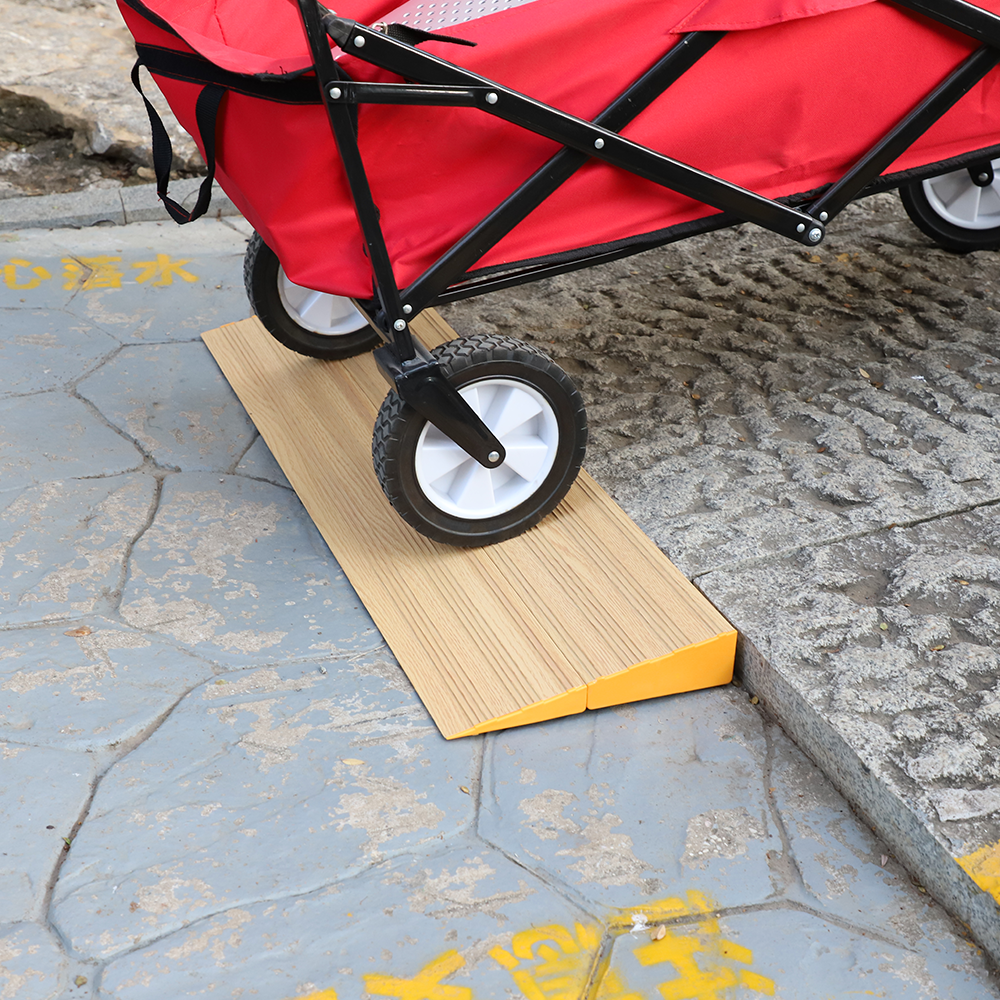 A close-up of a red utility cart moving over a wooden threshold ramp positioned on a slightly uneven outdoor surface.