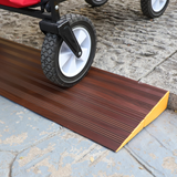 A close-up of a utility cart wheel moving over a brown aluminium threshold ramp with a yellow edge, highlighting the ramp's textured surface for grip.