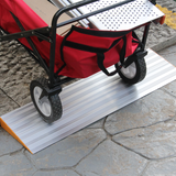 A red utility cart being pushed over a silver aluminium threshold ramp, positioned on a concrete outdoor path.