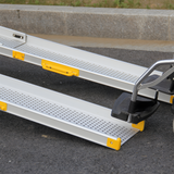 Close-up of Heeve aluminium telescopic mobility ramps with yellow handles, designed for wheelchairs. Ramps are positioned on an outdoor surface.