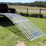 The Heeve 3m Aluminium Curved Folding Loading Ramp attached to a truck, extending to the ground for easy loading on grassy terrain