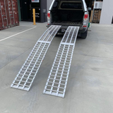 Pair of reinforced aluminium loading ramps extended from a pickup truck bed, ready for use in loading heavy equipment