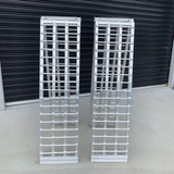 Two reinforced aluminium loading ramps standing upright side by side, showcasing their sturdy construction