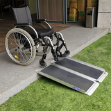 Wheelchair positioned on the Heeve aluminium single-fold ramp on a grassy outdoor step, illustrating its usability for wheelchair accessibility