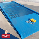 "Top-down view of the Heeve Forklift Low Dock Ramp, highlighting the grated surface for enhanced grip and the diamond plate entry section. A yellow safety locking mechanism with an attached chain is placed on the ramp. Labelled as 'Almost Perfect Items'."