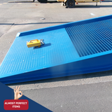 Image of the Heeve Forklift Low Dock Ramp featuring a durable grated surface and diamond plate entry section. The ramp is powder-coated in blue and includes a safety chain and yellow locking mechanism placed on top. Labelled as 'Almost Perfect Items