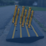 Six galvanised M10 anchor bolts arranged over a background featuring a black and yellow kerb ramp on a road with grass and pavement to the side.