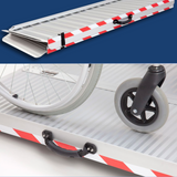 Close-up of a wheelchair wheel resting on a sturdy, portable aluminium ramp with red and white safety markings