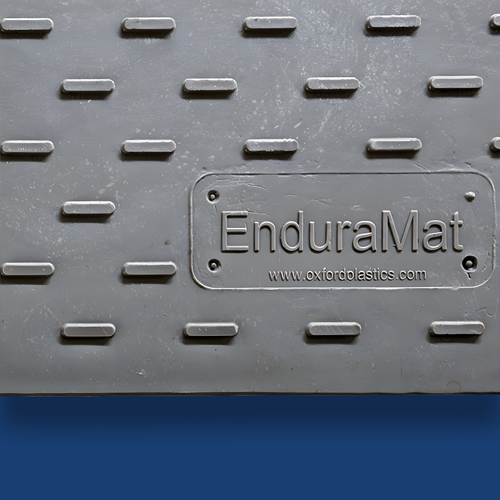 Close-up of a grey ground mat with the engraved label 'EnduraMat' from Oxford Plastics, featuring raised traction patterns