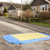 An outdoor scene featuring a complete LowPro 15/05 lightweight road plate installation across a residential road, indicating its effectiveness for road maintenance or construction work