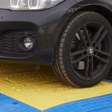 A close-up action shot showing a car tire crossing over the yellow section of the LowPro road plate, demonstrating the durability and load-bearing capability of the system.