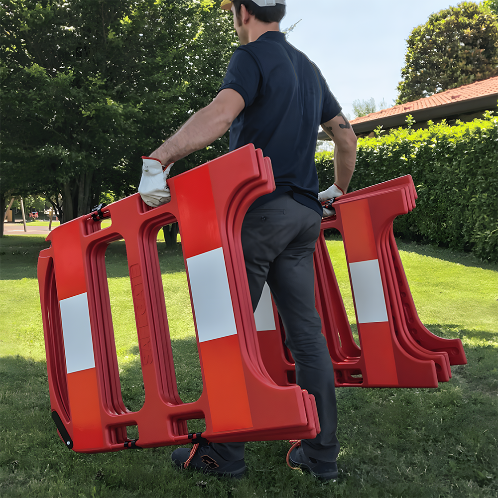 A man wearing gloves is carrying two lightweight red plastic barriers in an outdoor park setting