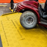 A mobility scooter safely using the yellow Supagrip Safekerb ramp, highlighting its robust and slip-resistant design.