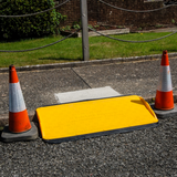 A yellow Supagrip Safekerb ramp positioned between two traffic cones on a sidewalk, ensuring pedestrian safety.