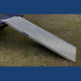 The ramp is shown in use, connected to a loading surface and placed on grassy terrain. This image demonstrates the ramp's practicality and ease of use in outdoor environments.